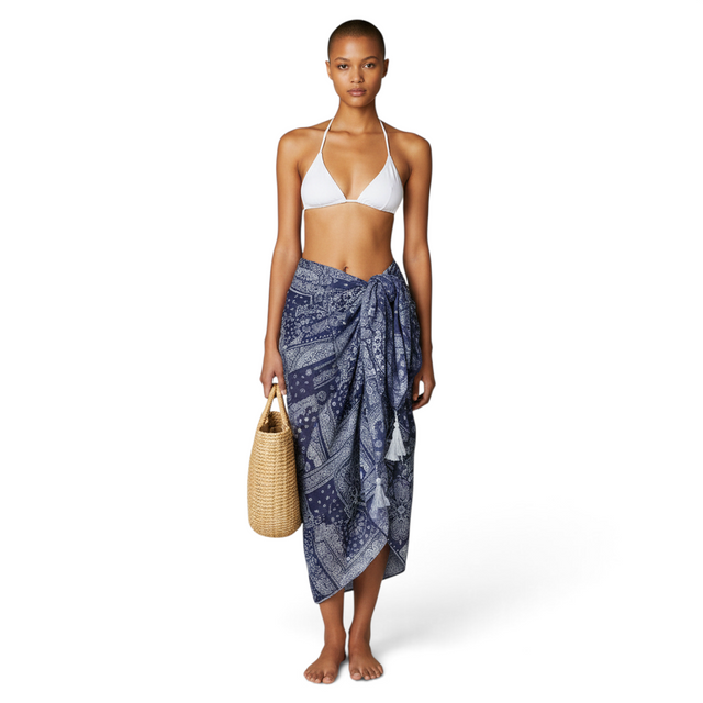 Model wearing a Mer St. Barth navy cotton bandana print pareo cover-up over a white bikini with a straw bag.