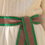 Mer St. Barth Emerald Bloom woven cotton belt with green and brown stripes and red tassels, cinching a white maxi dress.