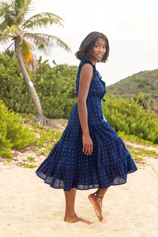 Mer St. Barth navy blue Swiss dot maxi dress with ruffle neckline and flutter sleeves worn by a woman on a beach.