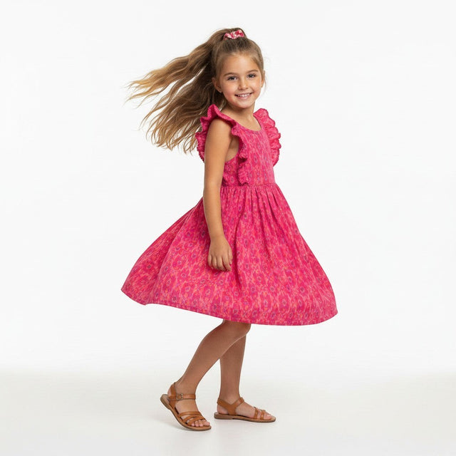 Young girl wearing a pink Mer St. Barth flutter sleeve dress with a rosette ikat print, spinning in a studio.