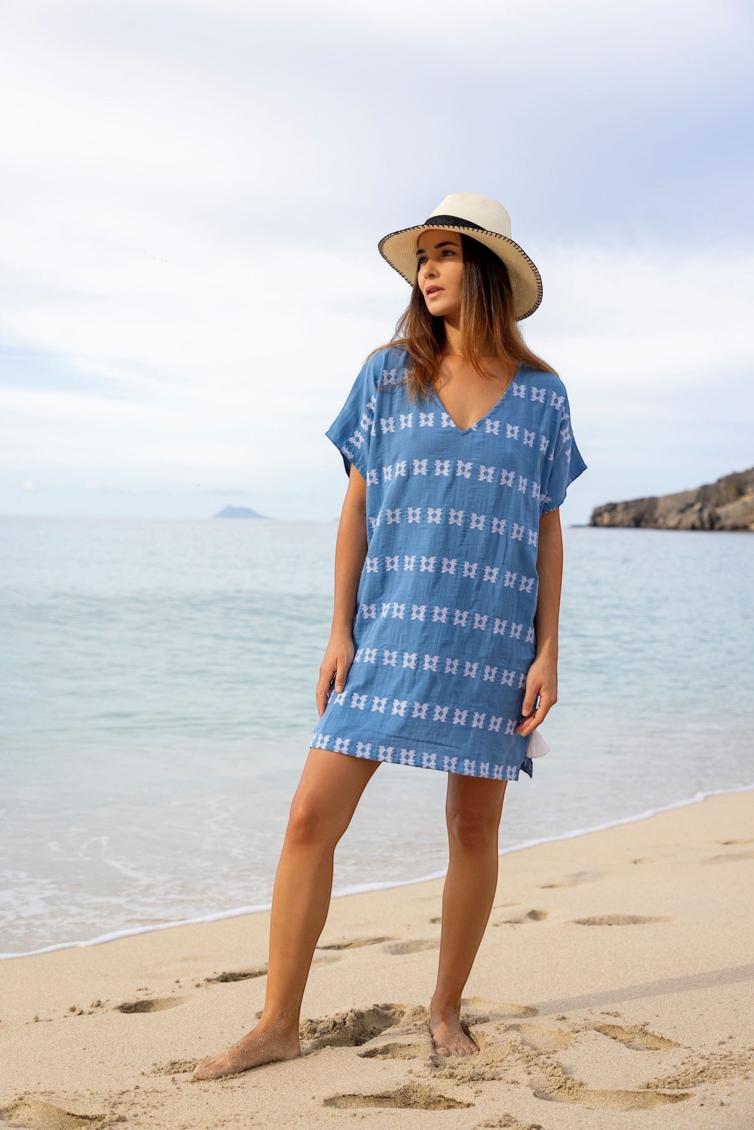 Mer St. Barth Capucine mini caftan in sky blue with white embroidery worn by a woman on a sandy beach