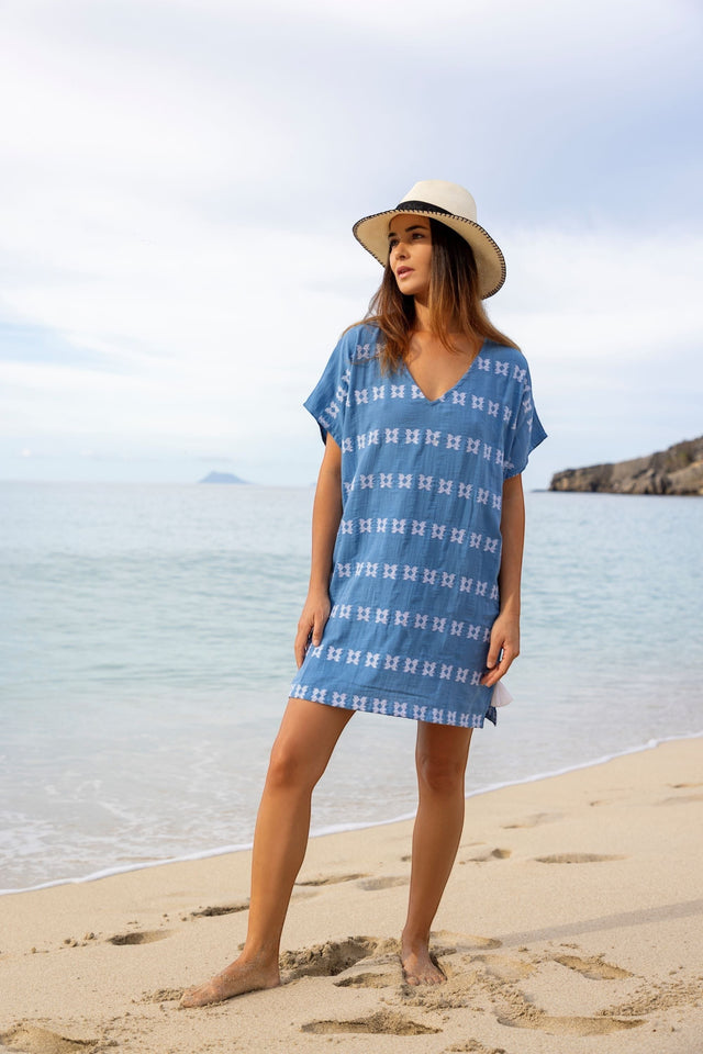 Mer St. Barth Capucine mini caftan in sky blue with white embroidery worn by a woman on a sandy beach